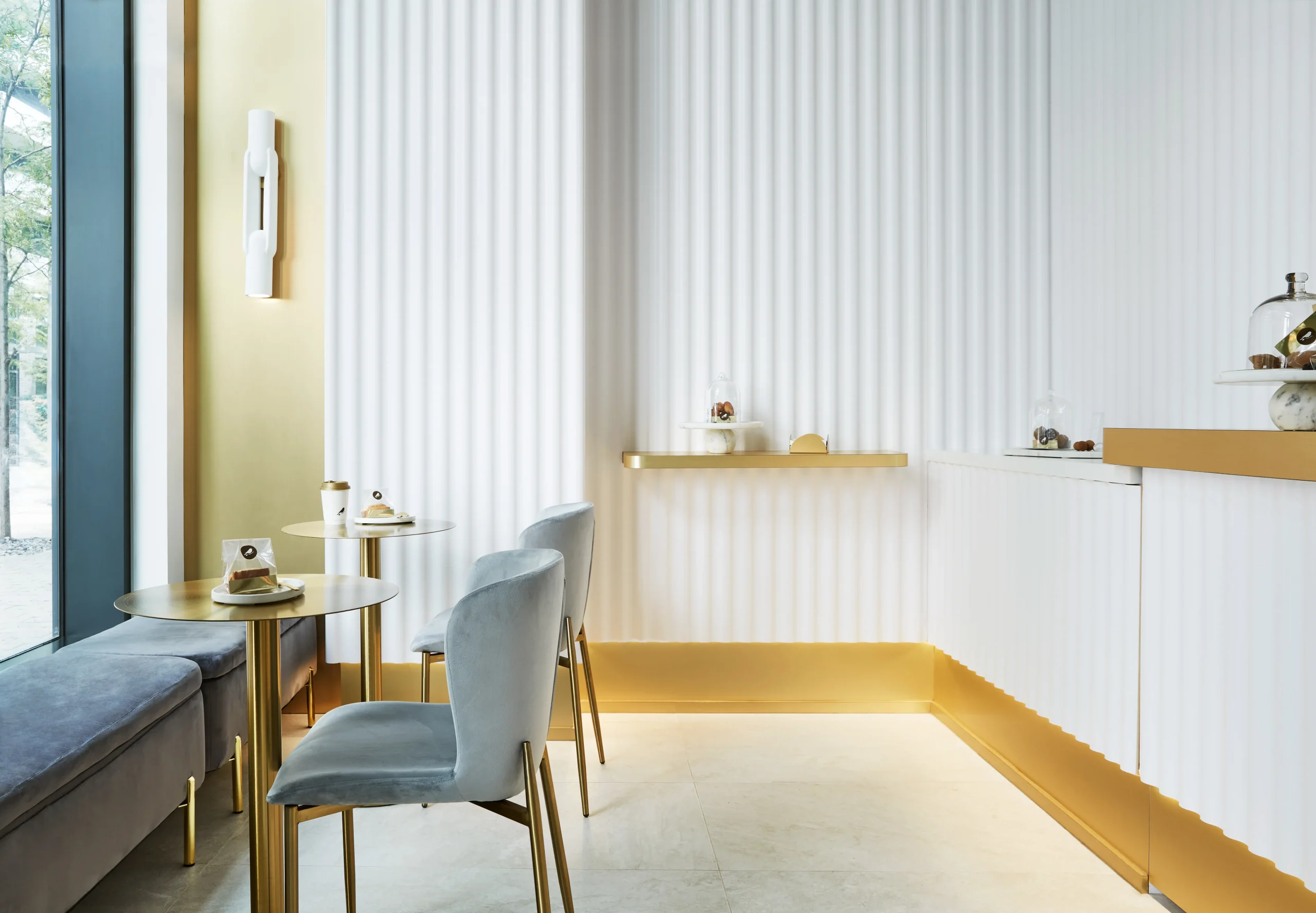 Interior Design - Interior view of a modern café featuring gold accents and textured white walls. Dexign Matter Studio
