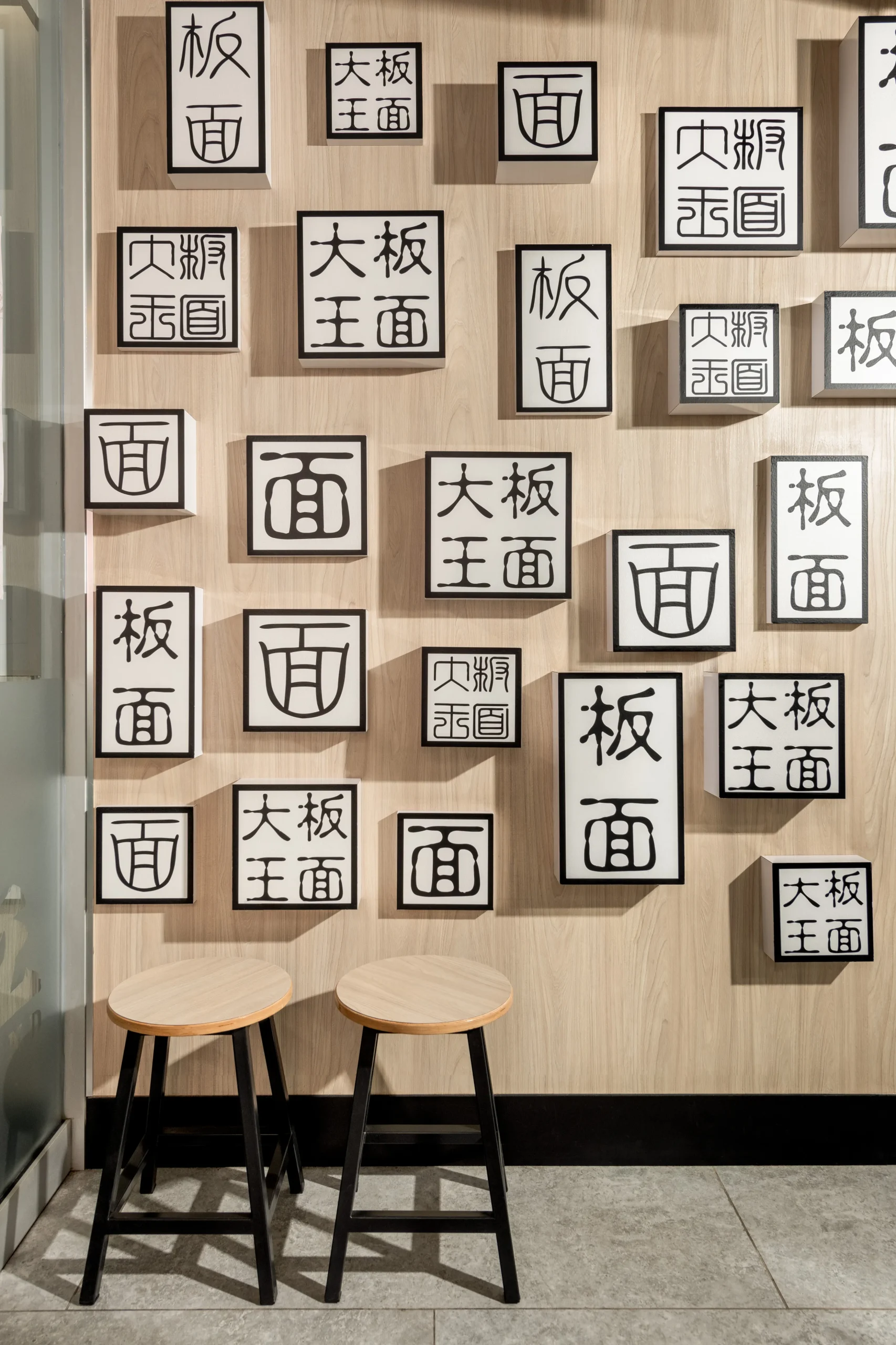 Interior Design - Wall featuring decorative boxes with Chinese characters and two wooden stools in front. Dexign Matter Studio