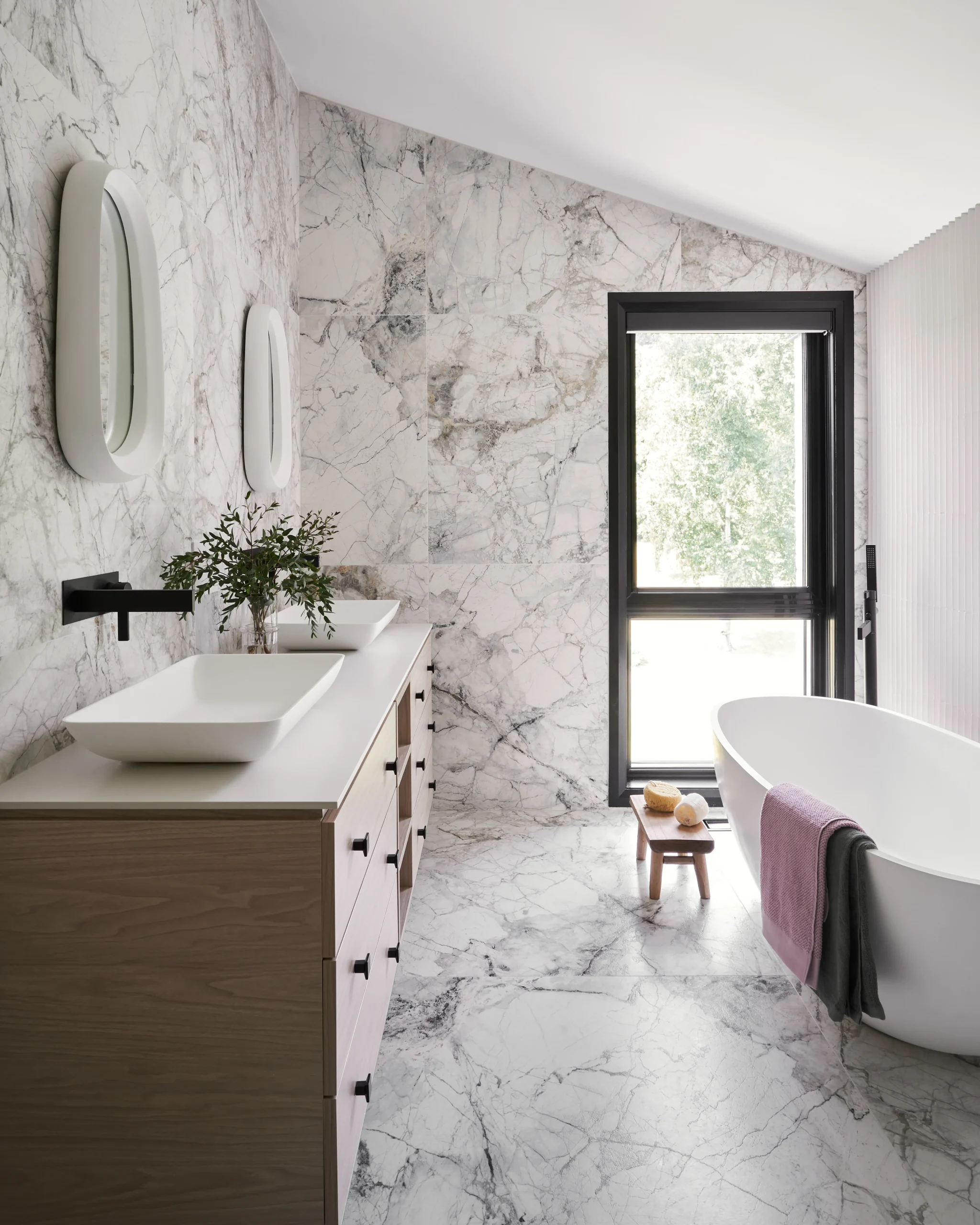 Interior Design - A modern bathroom featuring marble walls, a freestanding bathtub, and a wooden vanity with mirrors. Dexign Matter Studio