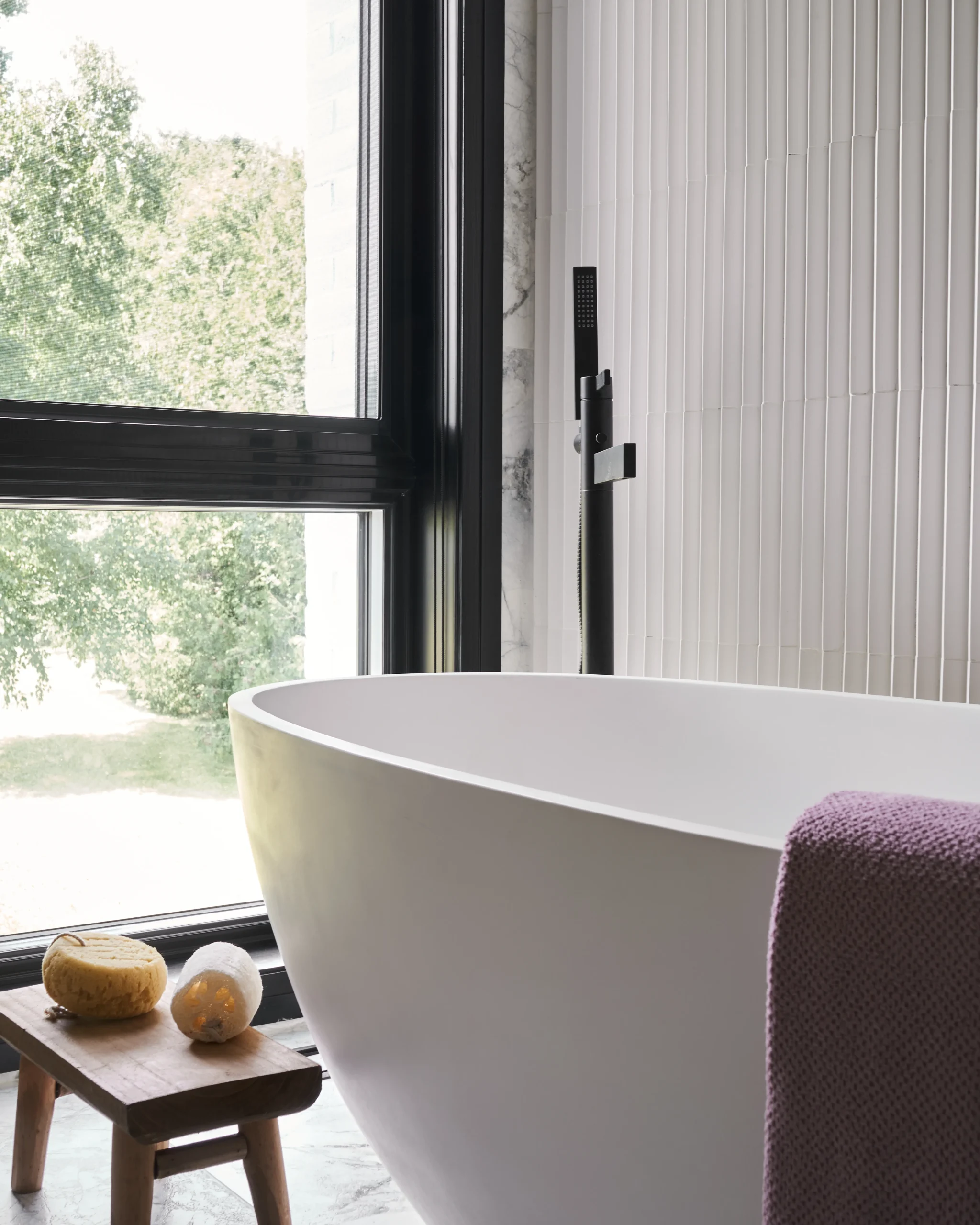 Interior Design - A modern freestanding bathtub with a purple towel and bath accessories on a wooden stool. Dexign Matter Studio