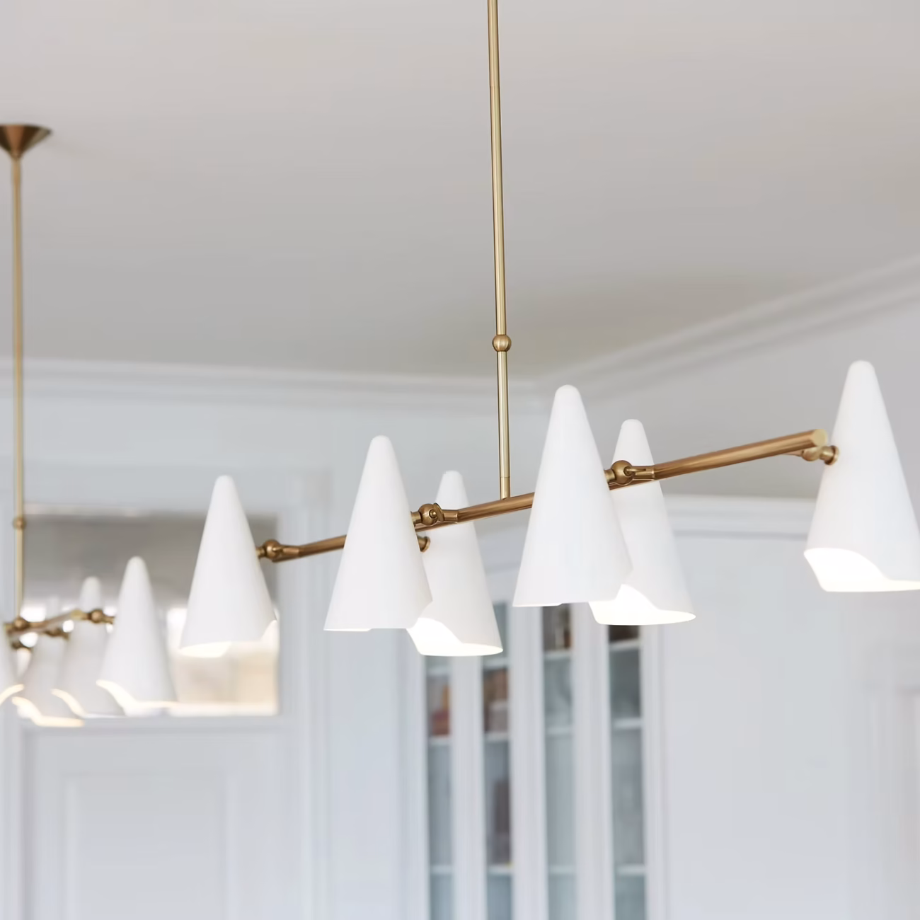 Interior Design - A modern pendant light fixture with white cone-shaped shades and a gold frame, hanging from the ceiling. Dexign Matter Studio
