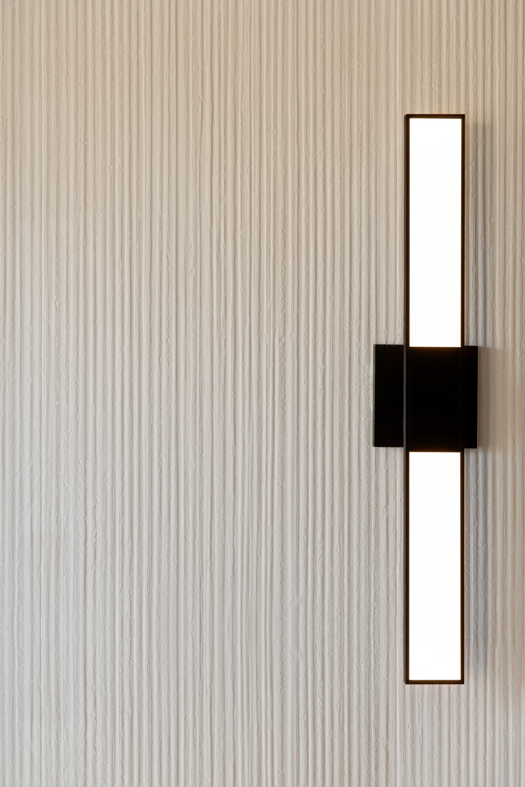 Interior Design - A modern wall sconce with a vertical light fixture mounted on a textured wall. Dexign Matter Studio