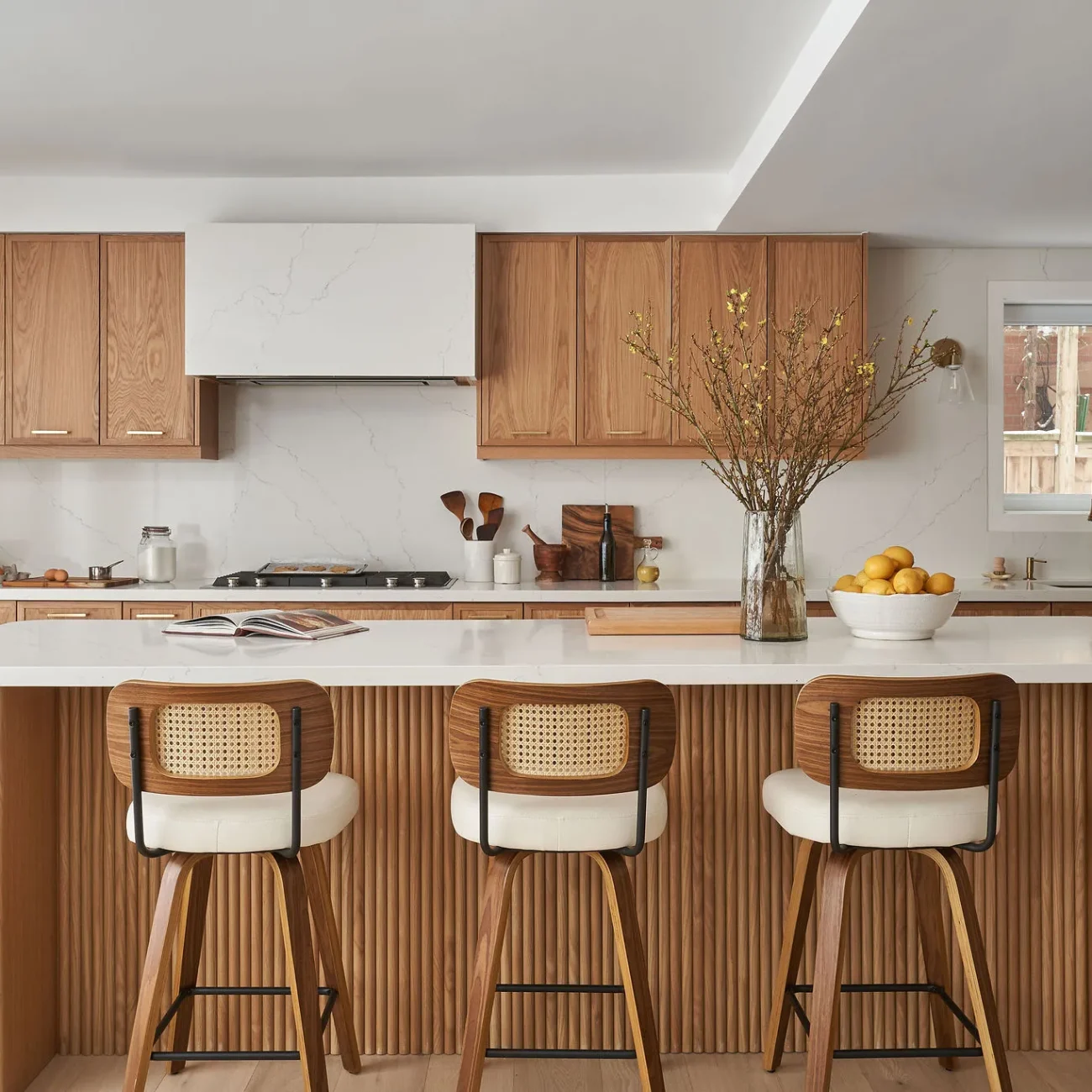 Interior Design - Contemporary kitchen featuring wooden cabinets, a white countertop, and bar stools with a decorative vase. Dexign Matter Studio
