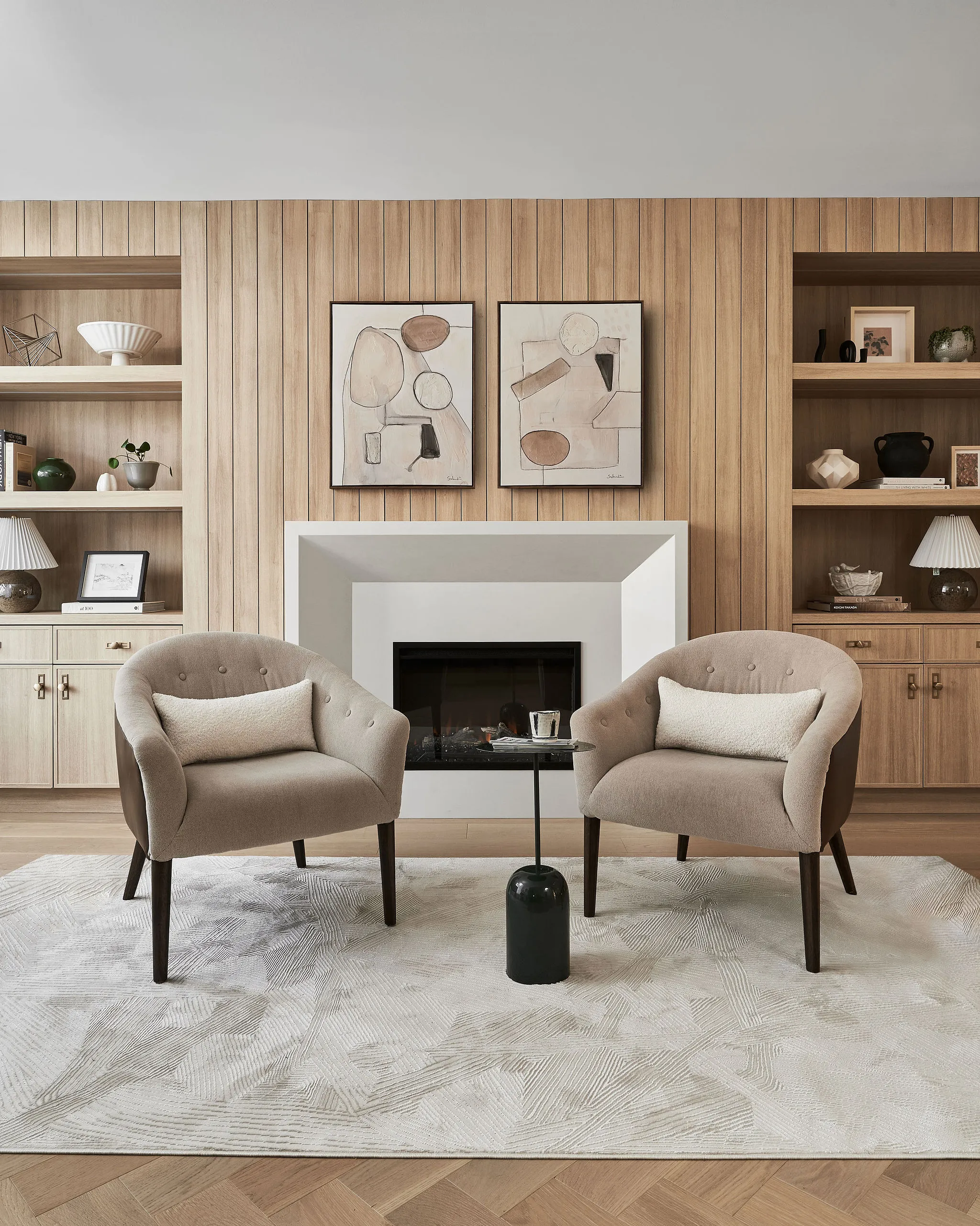 Interior Design - Two beige armchairs positioned in front of a fireplace with abstract art on the wall. Dexign Matter Studio