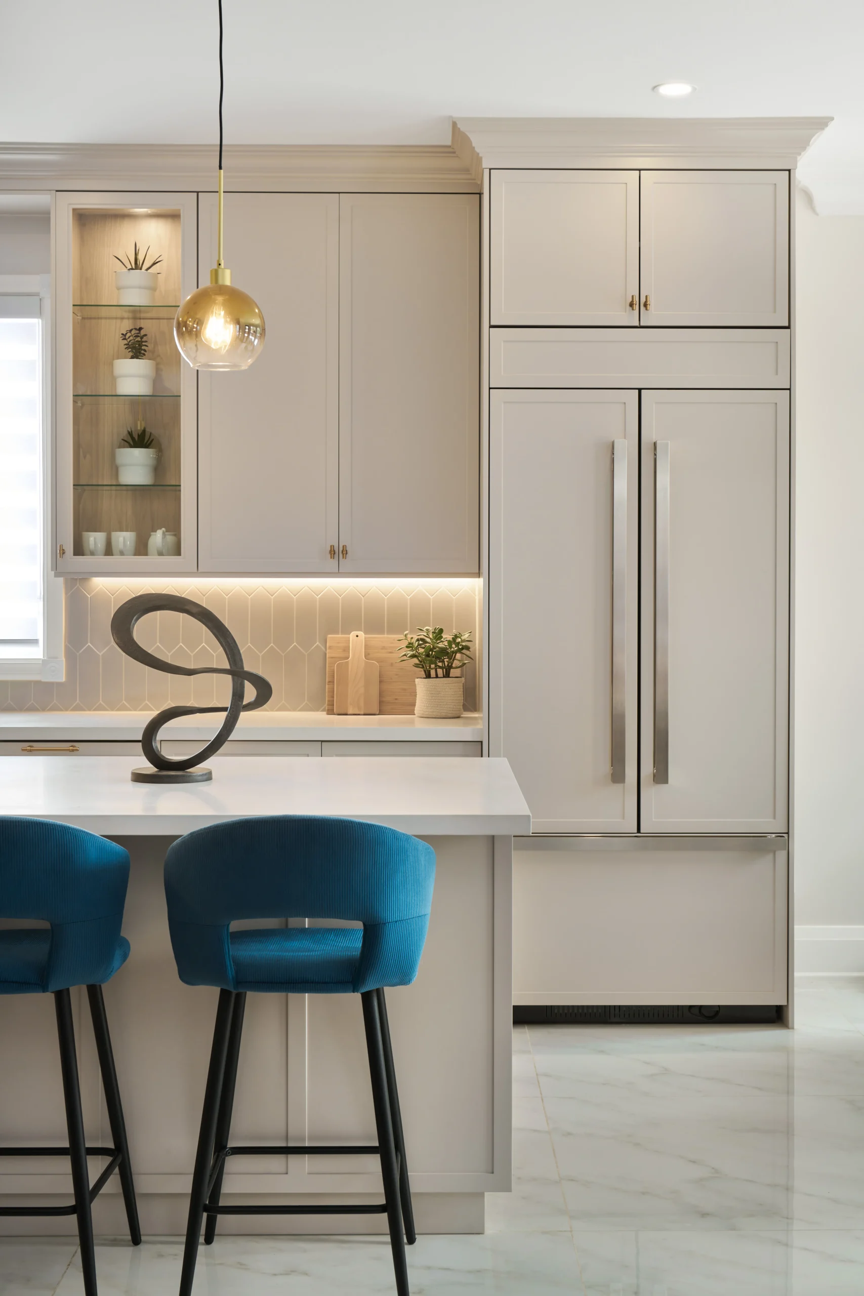 Interior Design - Modern kitchen featuring blue bar stools, light cabinetry, and decorative items on display. Dexign Matter Studio